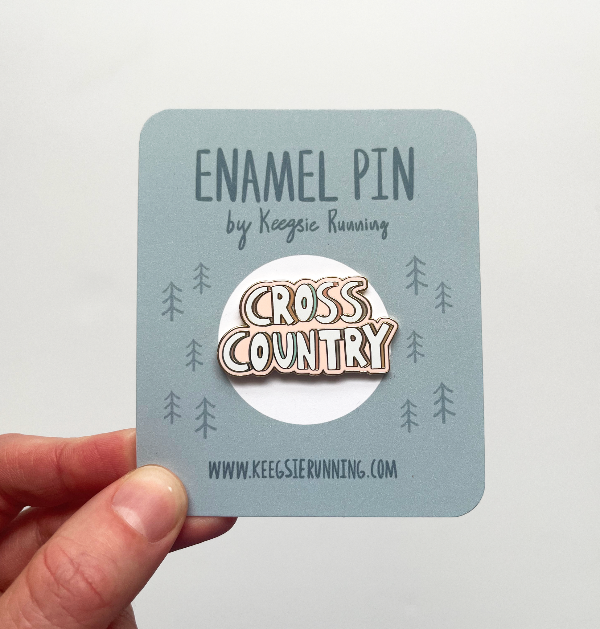 cross country enamel pin attached to backing card being held in hand
