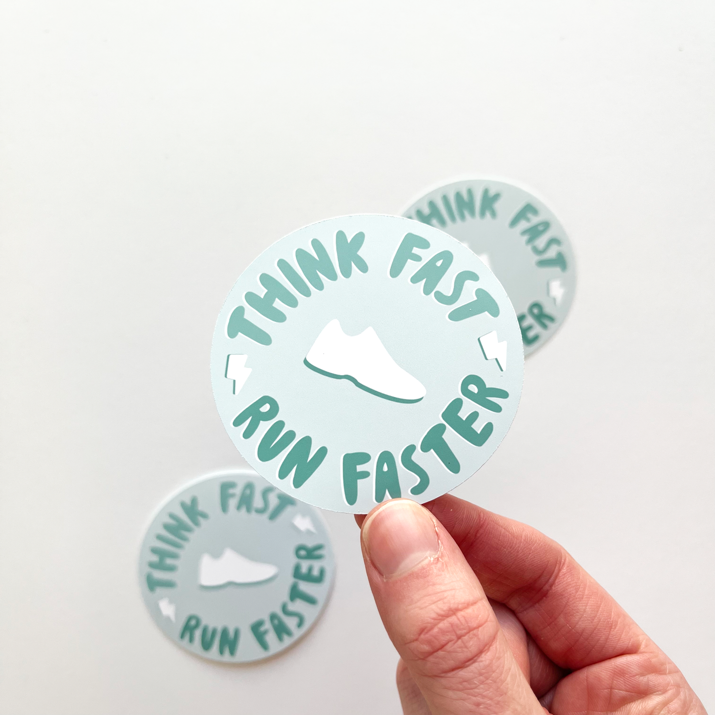 Think fast run faster sticker with text wrapped around the edge of a circle in teal text. White shoe in the center of the light blue circle. 