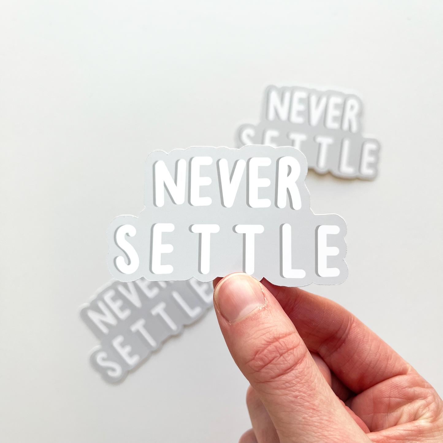 Never settle sticker with white text and a gray background