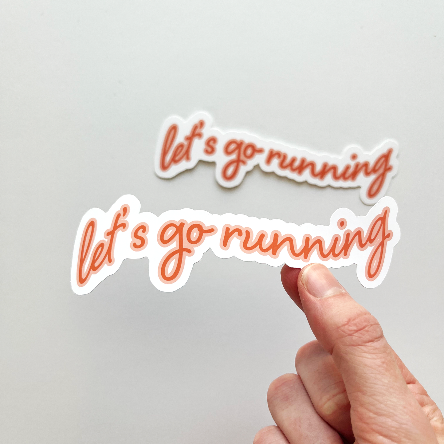 Let's go running sticker in deep orange text and a peach outline follow by white background