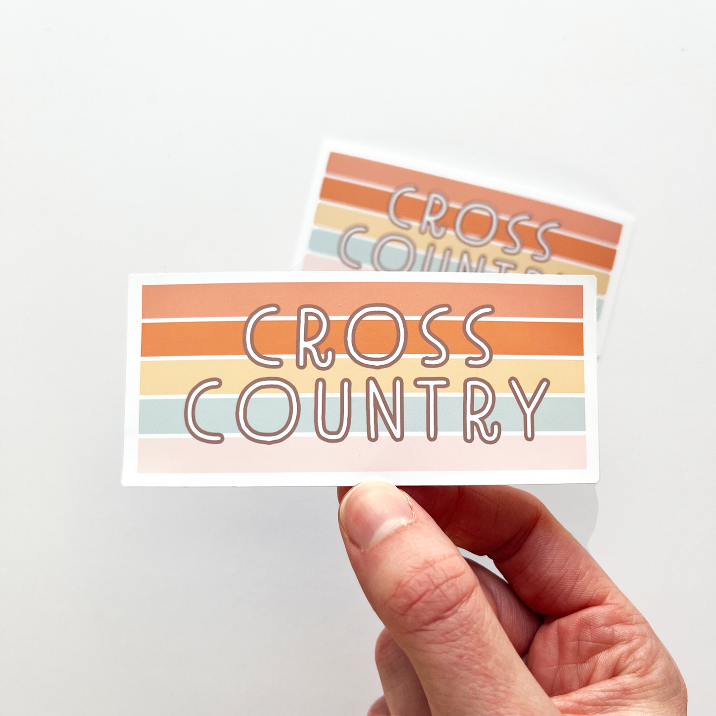Rectangular cross country sticker with horizontal stripes of peach, orange, yellow, light blue, and light pink