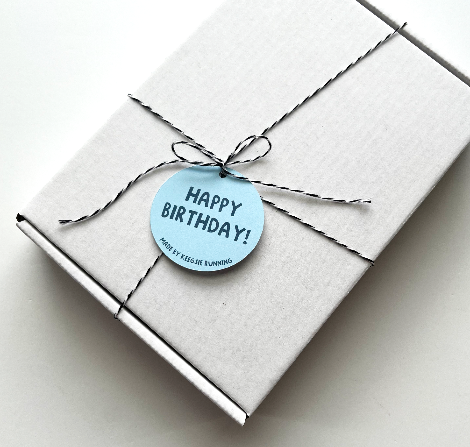 Runner birthday white gift box closed and tied with twin and tag that says "happy birthday! made by keegsie running"