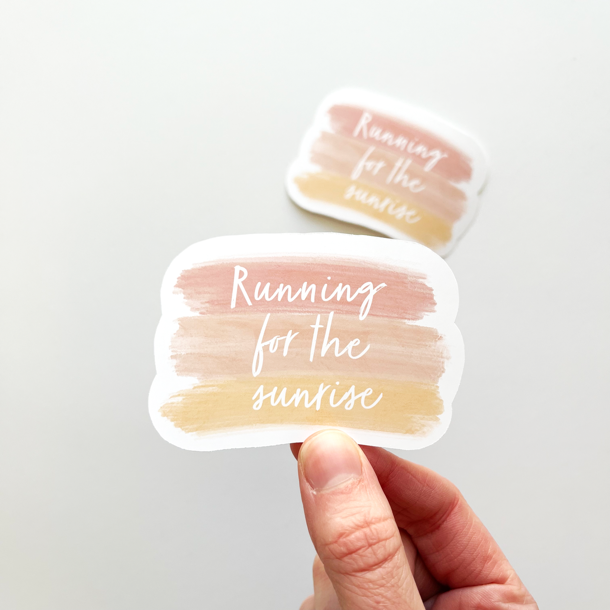 Running for the sunrise sticker in white text with paint strokes as the background in colors of pink and yellow